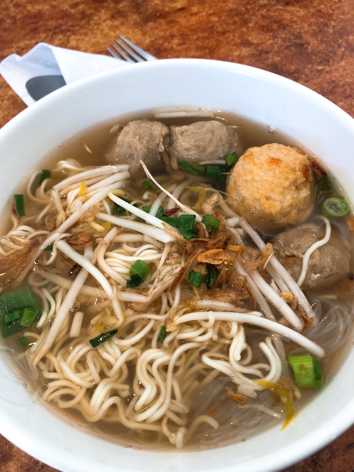 A bowl of noodle soup with meatballs, bean sprouts and fried shallots